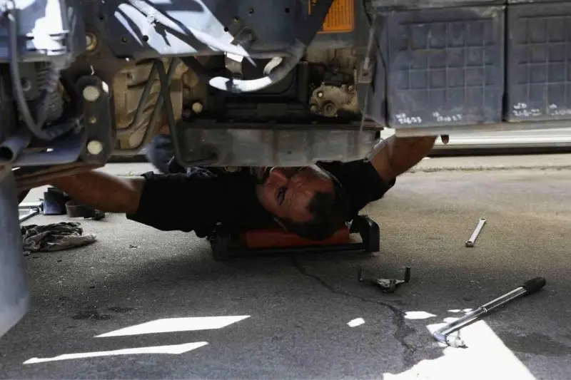Mechanic repairing under vehicle in workshop.