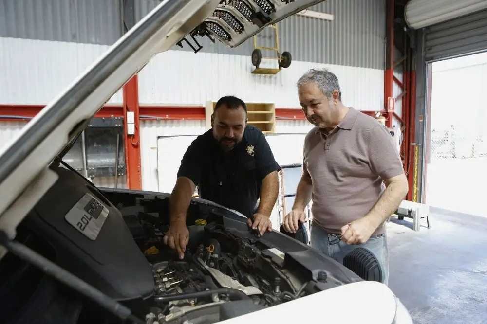 Mechanic showing car engine to customer in garage.