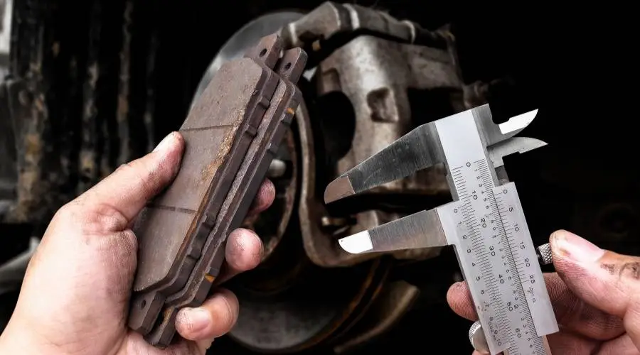 Brake pad thickness measurement using precision calipers showing minimum safe wear limits
