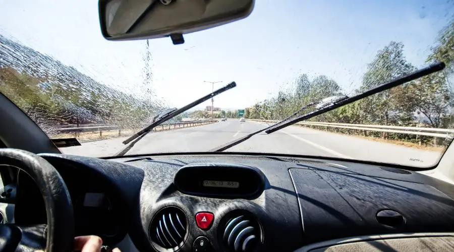 Driving with windshield wipers in action on sunny day.