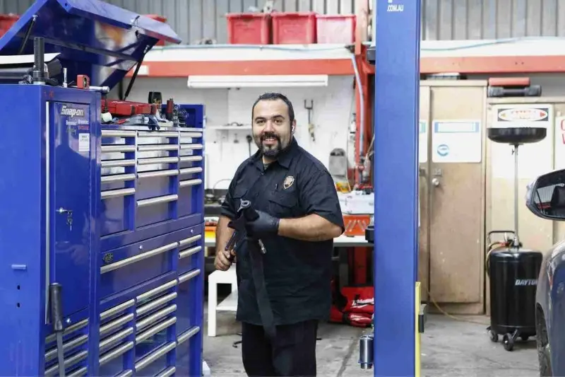 Mechanic smiling next to tool chest in workshop.