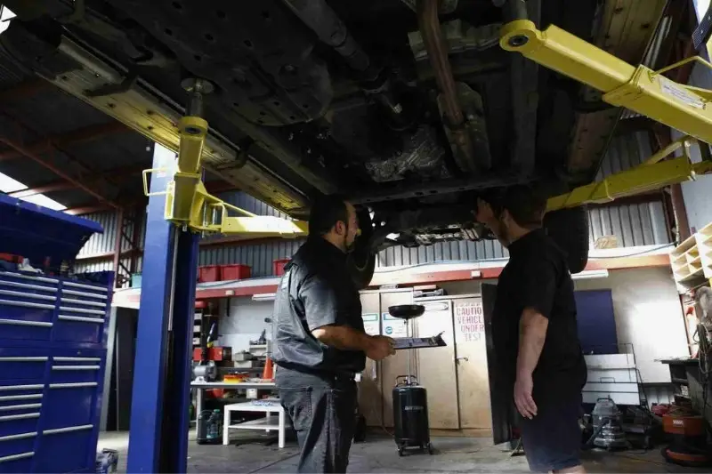 Mechanics inspecting car on hydraulic lift in garage.