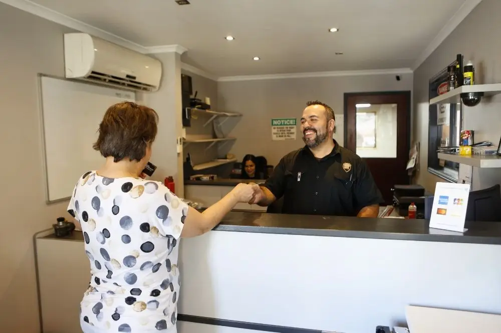 Receptionist shaking hands with a customer at desk.