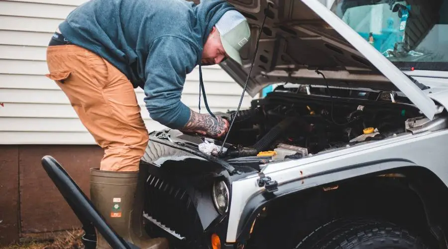 Man inspecting car engine in driveway.
