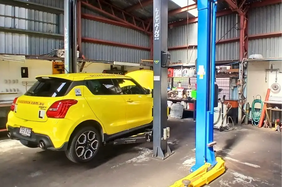 Yellow car on lift in repair shop.
