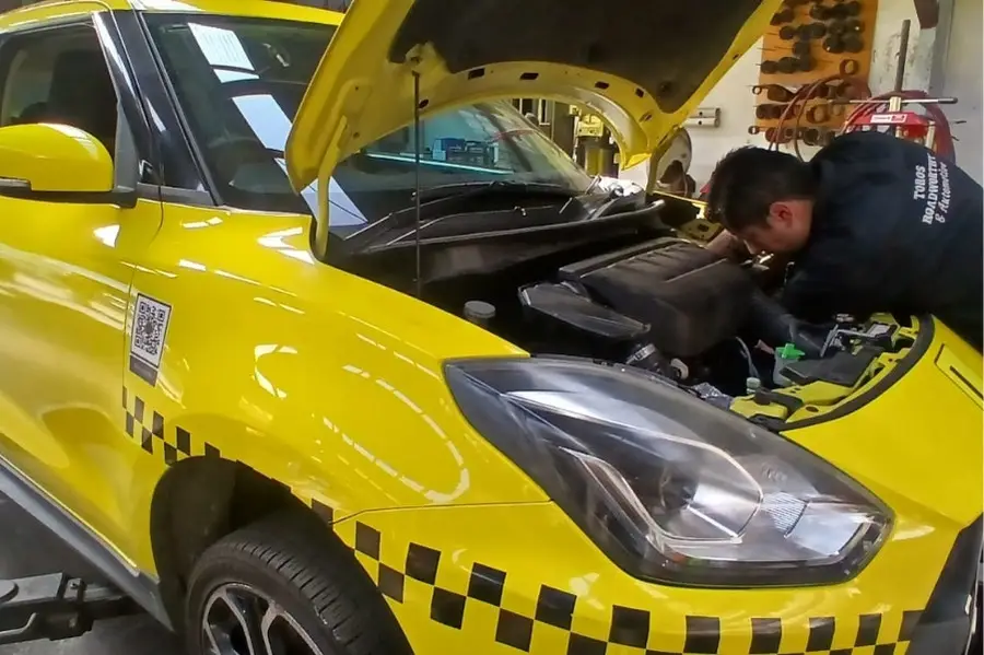 Mechanic repairing yellow taxi with open hood.